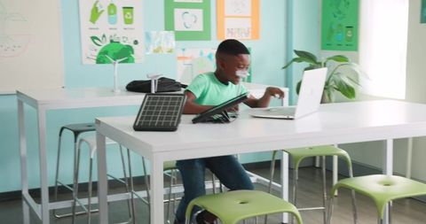 African American boy learning with laptop and solar panel in green makerspace classroom