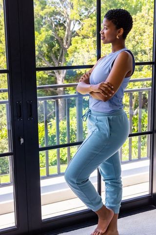 African american woman standing barefoot by black glass doors gazing at sunlit balcony