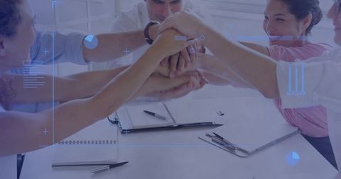 Stacking hands celebrating teamwork in meeting room with digital HUD overlay and notebooks