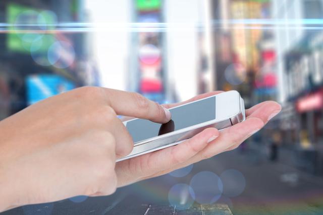 Composite image of hand holding smartphone and touching screen with street background 