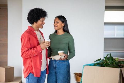 Couple Unpacking Boxes in New Home Holding Takeaway Coffee