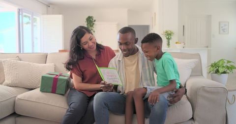 Family reading father's day card on sofa with gift box, cozy sunlit living room moment
