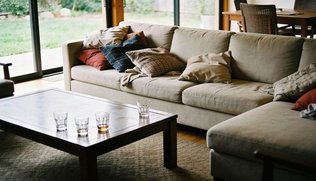 Sunlit living room showcasing beige sectional sofa with throw pillows and wooden coffee table