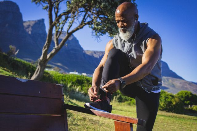 Senior African American man tying his shoe laces outdoors in a park. Ideal for promoting active senior lifestyles, fitness, health and wellness, retirement activities, and outdoor exercise routines.