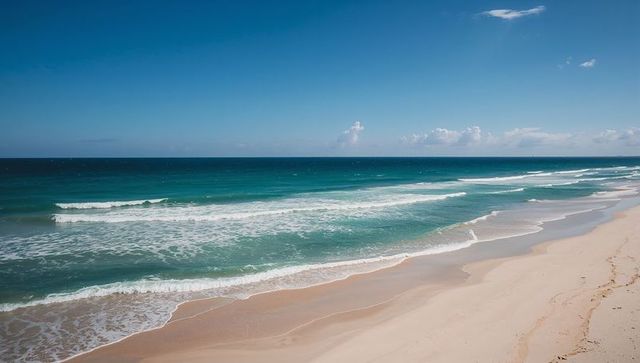Rolling turquoise surf meeting wide sunlit sand on calm horizon beach panorama seascape