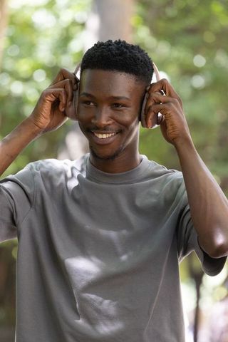 African american man adjusting over-ear headphones in park smiling and listening to music