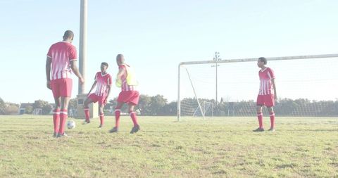 Youth soccer team practicing passing drills on sunlit grass pitch wearing red kits