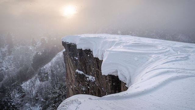 Overhanging Snow Cornice on Rocky Cliff at Foggy Sunrise, Windblown Sculpted Drifts