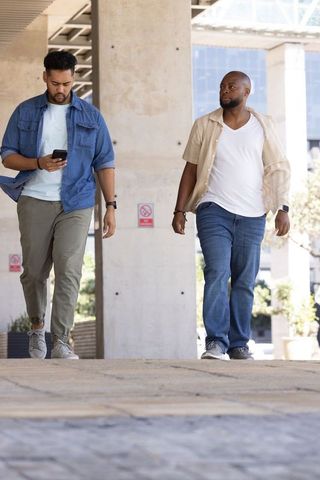 Two african american men walking urban walkway one using smartphone casual colleagues