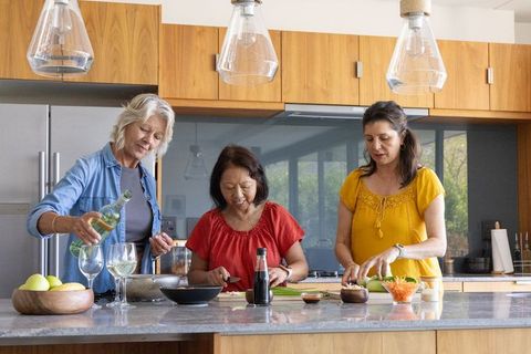 Multigenerational women cooking at kitchen island, chopping vegetables and pouring wine