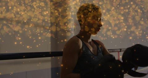 Golden bokeh silhouette of female boxer leaning in ring, focusing on strength and determination