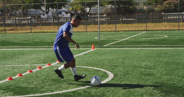 Biracial male football player wearing blue uniform training on outdoor pitch. Football, sports and fitness.