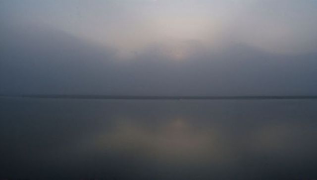 Hazy dawn reflecting on mirrorlike lake horizon minimal tranquil waterscape