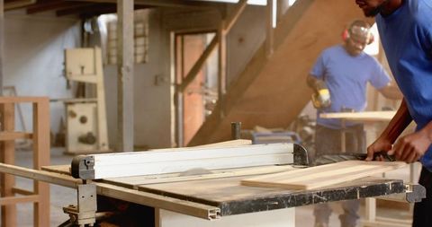 Men operating table saw in carpentry workshop crafting wood