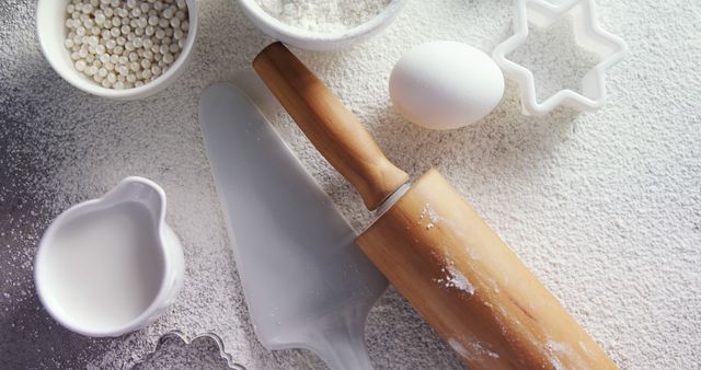 Baking ingredients and tools are neatly arranged on a countertop, with copy space. A rolling pin, whisk, egg, and cookie cutters suggest someone is preparing to make baked goods.