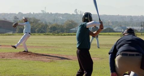 Amateur Baseball Game Pitcher Pitching Toward Batter with Umpire and Catcher on Sunny Field