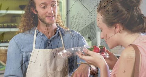 Market vendor offering clamshell of strawberries while customer smelling fresh produce