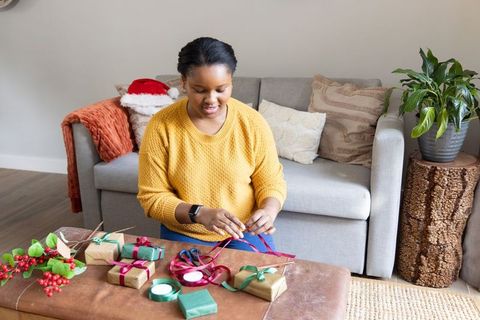 Wrapping holiday gifts on ottoman in cozy living room with african american woman