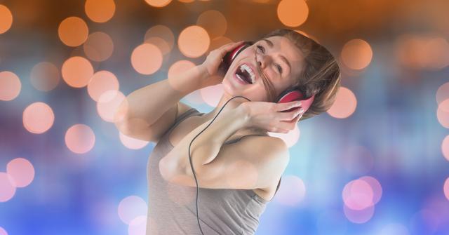 This image shows a joyful woman wearing headphones, enjoying music with a vibrant bokeh background. Ideal for use in advertisements, music streaming services, lifestyle blogs, and social media posts promoting happiness, relaxation, and entertainment.