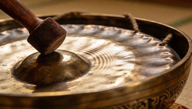 Brass singing bowl being struck with padded mallet producing rippling sound and vibration