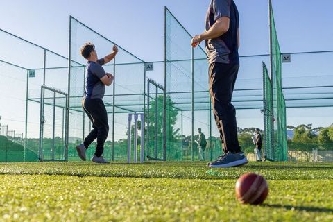 Cricket players practicing bowling in outdoor nets at professional training facility