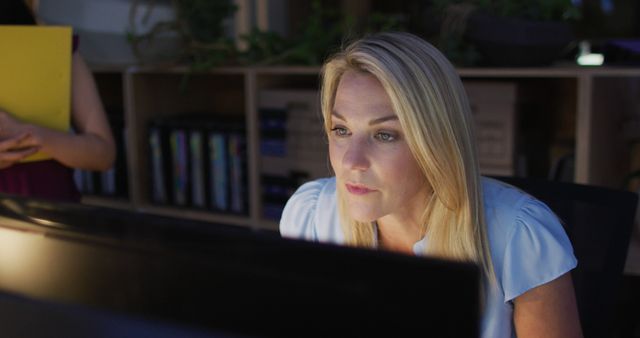 Image of focused caucasian woman using computer, working late in office. Business and working in office at night with technology concept.