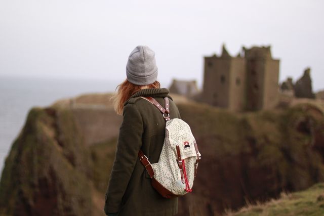 Woman with backpack exploring coastal cliff ruins during winter. Useful for travel blogs, tourism advertisements, or adventure magazines.