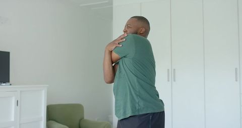 African man stretching shoulders in bright minimalist living room morning home stretch