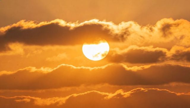 Golden sun rising through layered clouds casting warm amber light over hazy horizon