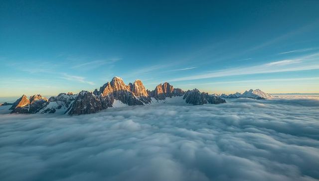 Alpine jagged mountain ridge rising above sea of clouds at golden alpenglow panorama
