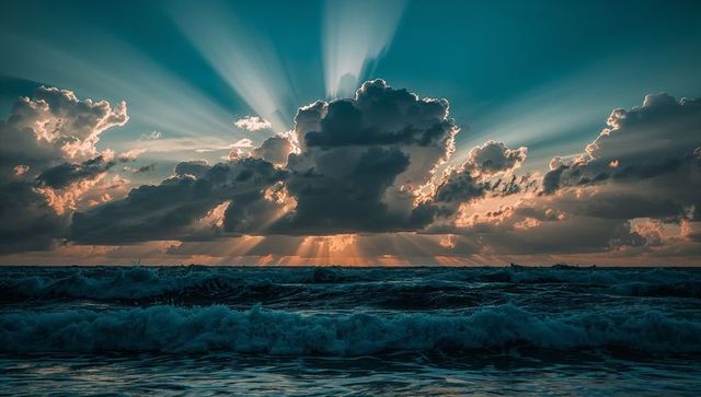Dramatic Sunrise with Sunbeams and Turbulent Ocean Waves