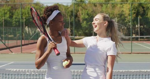 Female Tennis Partners Laughing and Hugging at Net on Sunny Hard Court Showing Friendship