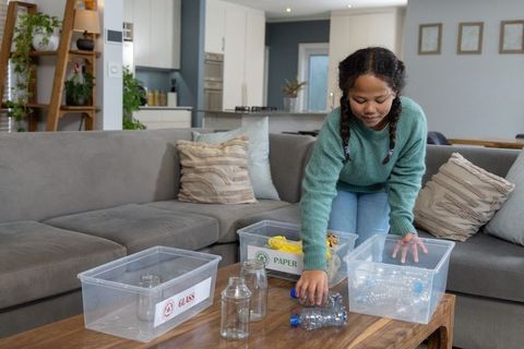 Girl sorting recyclables on coffee table in cozy living room teaching sustainable habits
