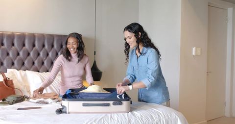 Diverse friends packing in cozy bedroom for exciting travel adventure
