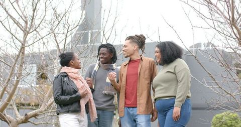 Diverse friends laughing and chatting on rooftop courtyard wearing scarves and jackets