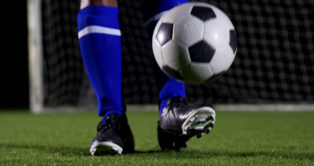 Soccer player wearing blue socks and black shoes is dribbling a soccer ball on a field at night. Ideal for articles, sports event promotion, athletic advertisements, soccer training materials, or sports equipment catalogs.