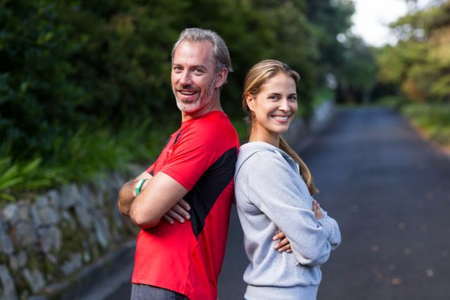 Smiling athletic couple standing back to back on the open road