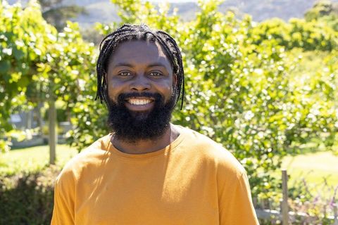 African american man smiling in sunlit garden wearing mustard shirt