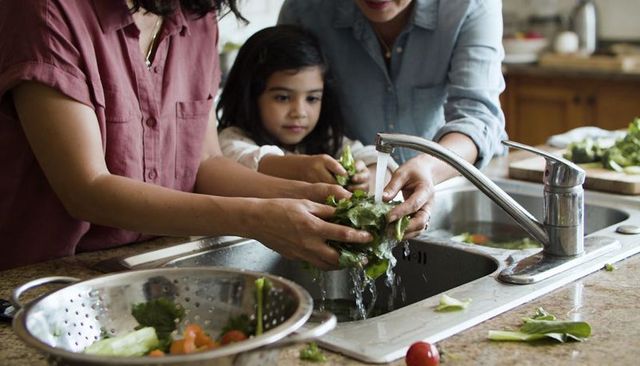 Family washing fresh salad greens together at kitchen sink, teaching kids healthy habits