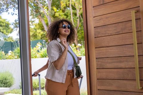 African american woman walking into modern home pulling suitcase through sunlit wooden door