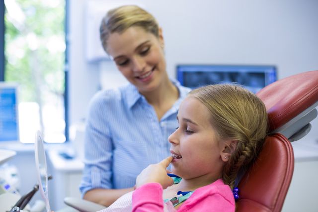 Young girl sitting in dental chair looking in mirror while dentist observes. Ideal for illustrating pediatric dentistry, dental checkups, and oral health education. Can be used in healthcare brochures, dental clinic websites, and educational materials about children's dental care.
