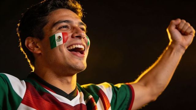 Triumphant mexican soccer fan cheering with face paint and raised fist, rim light