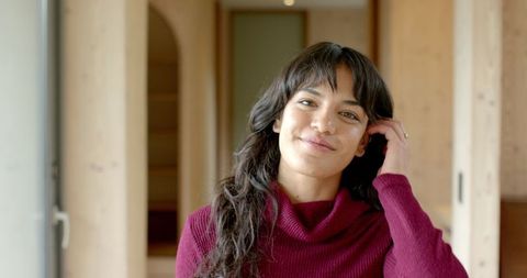 Woman in Wood Paneled Room Wearing Burgundy Sweater, Touching Hair