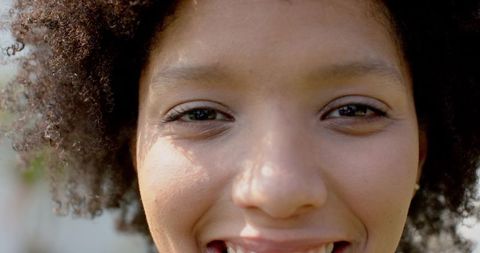 Sunlit close-up of smiling woman with curly hair looking at camera, natural beauty portrait