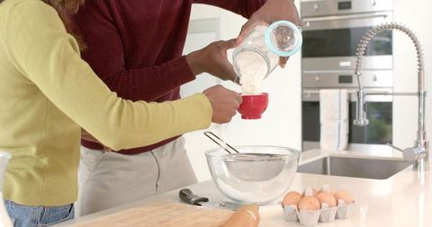 Diverse couple pouring and sifting flour on modern kitchen island, baking together