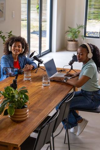 African american women recording podcast in modern home studio with laptop and microphones