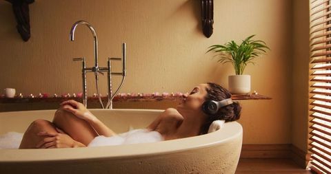 Woman relaxing in spa bath with headphones and foam