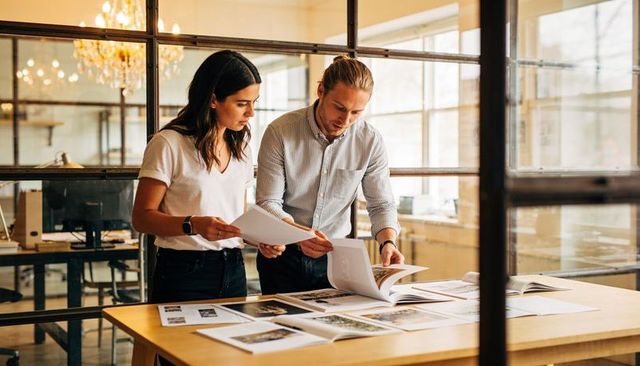 Creative team reviewing print layouts and portfolio in sunlit modern office studio
