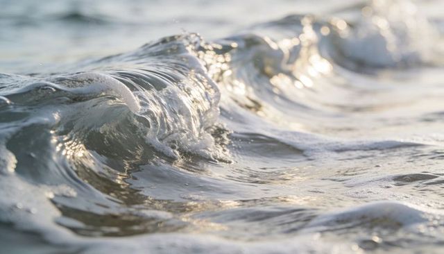 Sunlit wave crest rolling over shallow shoreline with shimmering foam and wet sand texture