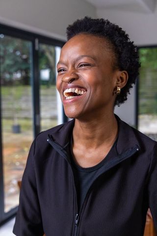 African american woman laughing by glass doors in modern home wearing black zip jacket
